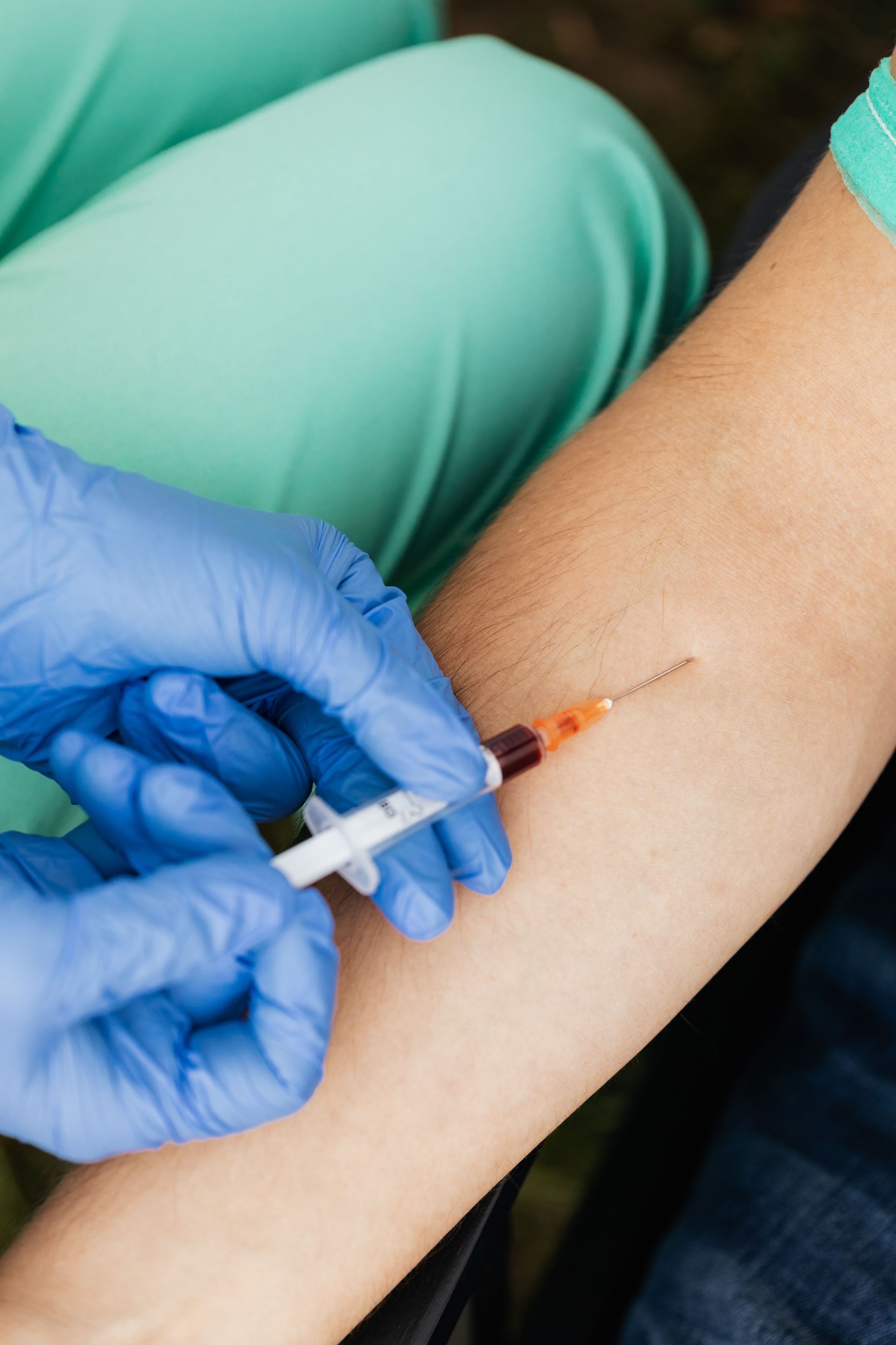 A healthcare professional performs a blood draw using a syringe and gloves. Focus on hands.