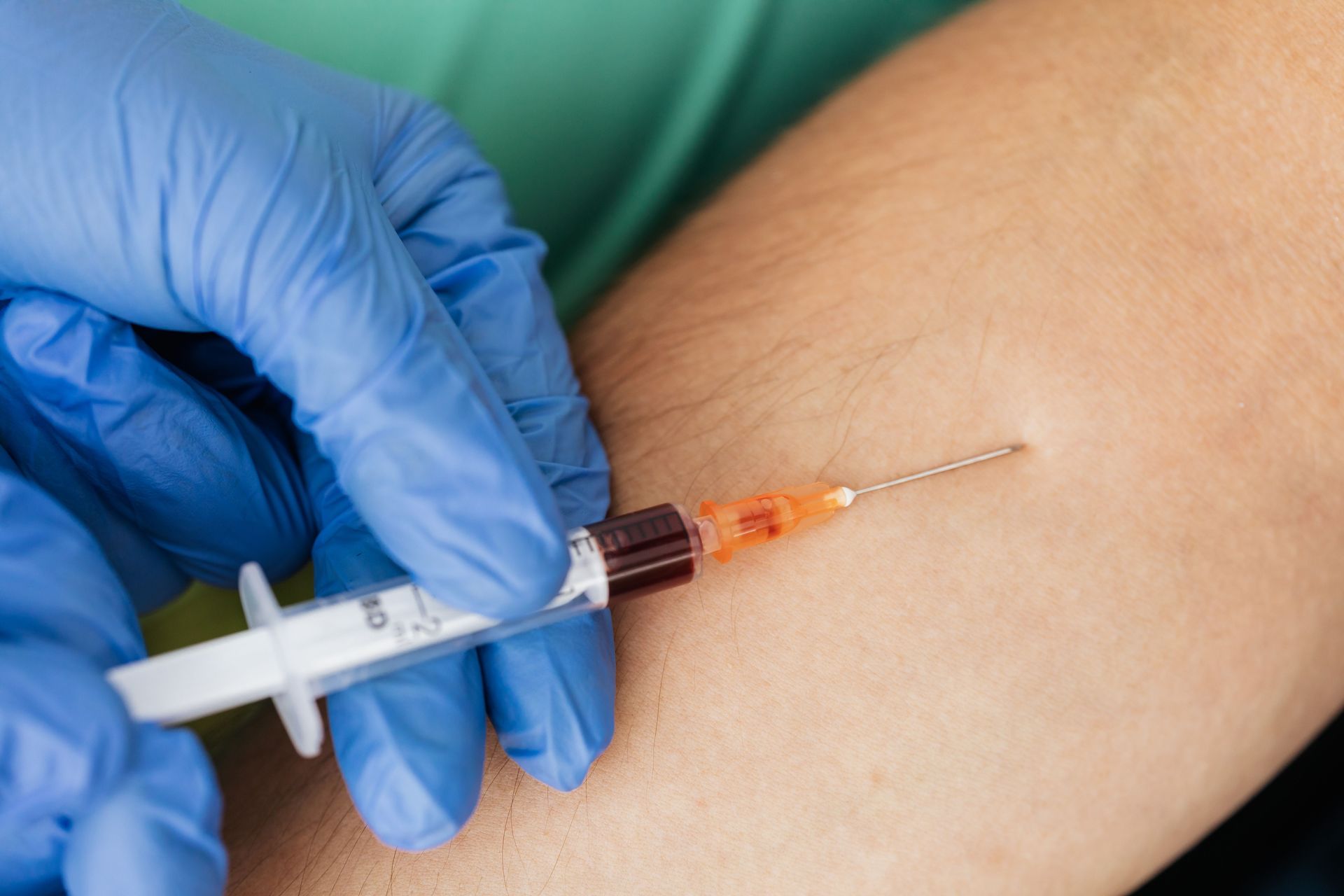 Close-up of a healthcare professional wearing gloves using a syringe for blood extraction.