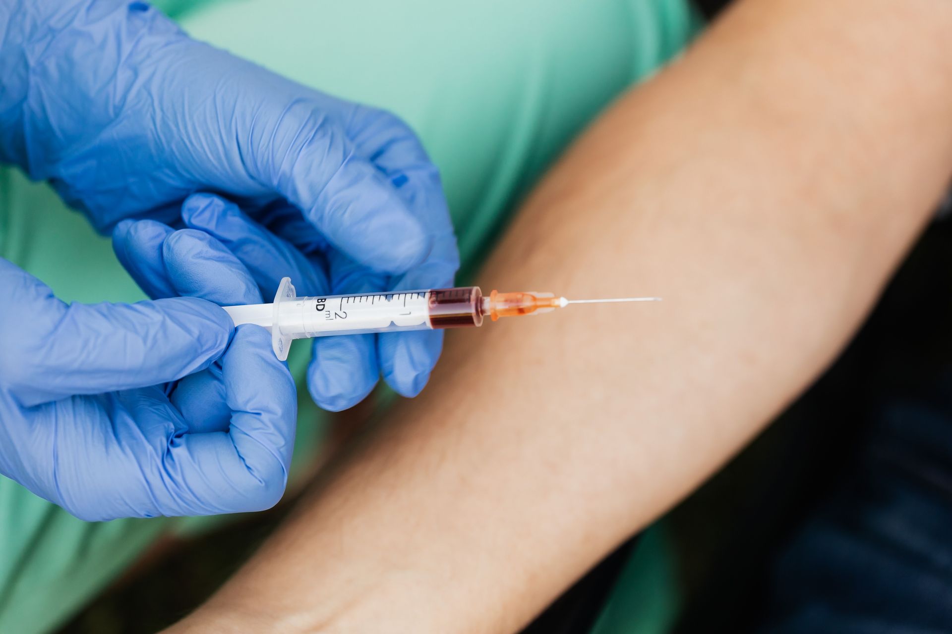 Medical professional using syringe for blood extraction with latex gloves.